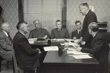 The original Mennonite Mutual Aid board, September 1950. L-R: John I Yoder, Harry Diener, Simon Gingerich, Orie O. Miller, Aaron Herr (staff), Chris L. Graber (standing), Guy F. Hershberger. Scan courtesy Archives of Mennonite Church USA-Goshen.